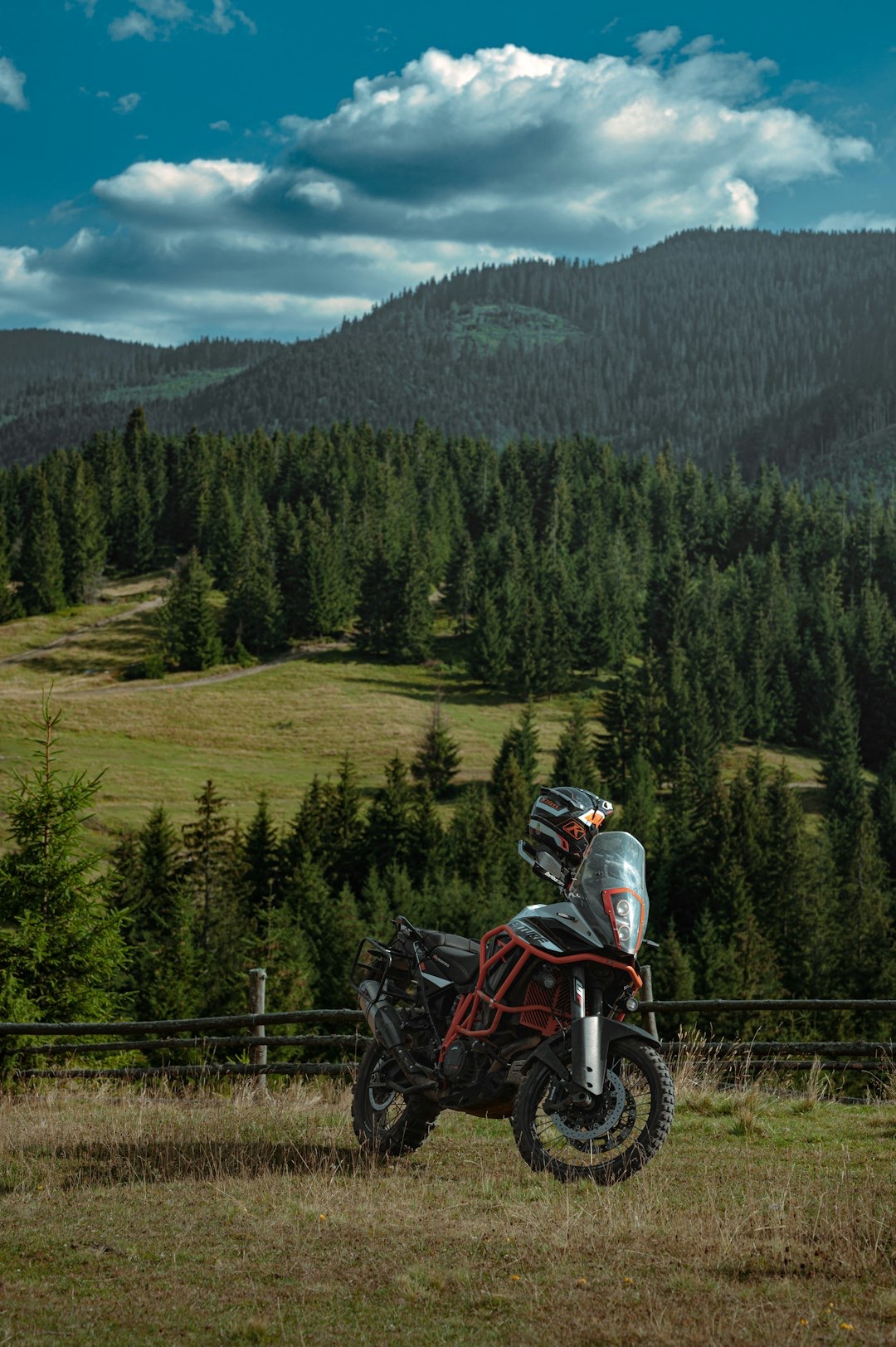 Adventure motorcycle parked on a grassy hillside before mountain forests.